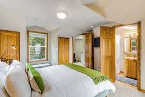 A bedroom with a bed, a window, a door, and a bathroom visible through an open door.