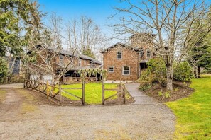 A two-story wooden house with a gravel driveway and a wooden fence.