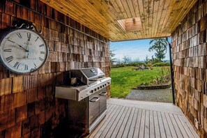 A wooden deck with a barbecue grill and a wall-mounted clock. - Stunning waterfront 3BR with firepit & woodstove (Camano Island)