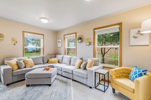 A living room with a sectional sofa, a small table, and a yellow armchair. - Stunning waterfront 3BR with firepit & woodstove (Camano Island)