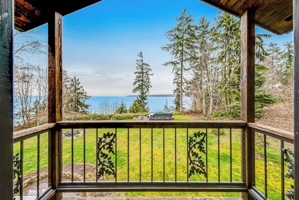 A wooden deck with a railing, overlooking a grassy area with trees and a body of water in the distance.