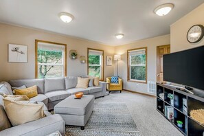 A living room with a sectional sofa, a coffee table, a TV, and a bookshelf.