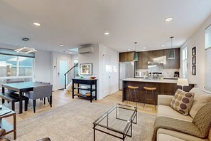 A modern living room with a glass coffee table, a sofa with patterned cushions, and a dining area with a dark wooden table and chairs. - 2BR modern house, private backyard, fireplace, BBQ (Seattle)