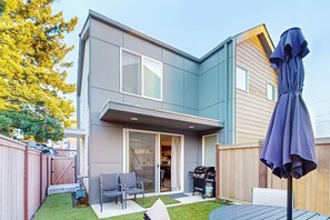 A modern two-story house with a patio area, a barbecue grill, and a covered seating area. - 2BR modern house, private backyard, fireplace, BBQ (Seattle)