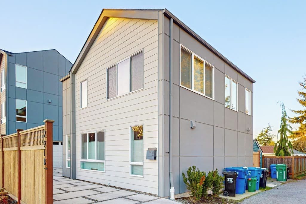 A modern two-story residential building with a sloped roof, large windows, and a visible electrical box on the exterior wall.