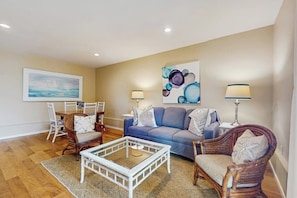 A living room with a blue sofa, wicker chairs, a glass coffee table, and two floor lamps.