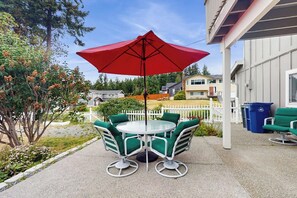 Eine Terrasse mit rundem Tisch und Stühlen, einem roten Sonnenschirm und einem weißen Zaun.
