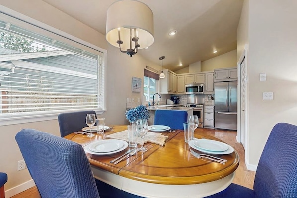 A dining area with a round table, chairs, and a kitchen in the background.