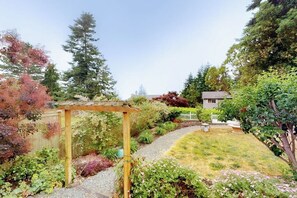 A garden with a wooden pergola, a gravel path, and a variety of plants.