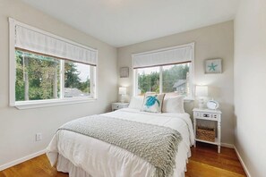 A bedroom with a bed, two bedside tables, a nightstand, and a window with a view of trees.