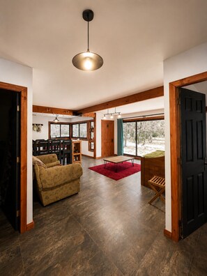 A spacious living area with a sofa, a coffee table, and a dining table. There is a large window providing a view of the outdoors. - Refugio frente al Volcán Llaima, sector captren, curacautin. (Curacautin)