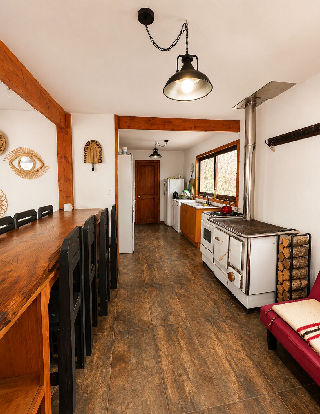 Une cuisine avec une table en bois, des chaises, un poêle et un luminaire suspendu.