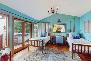 Ein Schlafzimmer mit zwei Betten, einem Schreibtisch, einem Stuhl, einer Kandelaberleuchte und einem großen Fenster mit Vorhängen.