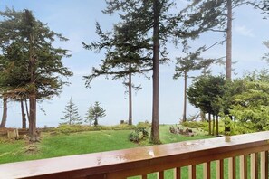Eine Holzterrasse mit Blick auf eine Wiese, hohe Bäume und einen klaren Himmel.