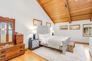 A bedroom with a wooden ceiling, a bed with white bedding, a nightstand with a lamp, a dresser, and a mirror. - Lovely, open 3BR with water view & scenic deck (Seattle)