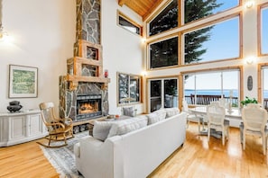 A spacious living room with a fireplace, a large sofa, and a dining area with chairs. - Lovely, open 3BR with water view & scenic deck (Seattle)