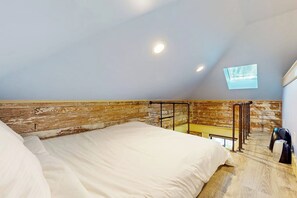 A bedroom with a sloped ceiling, a skylight, and a bed with white bedding. - Serene Studio 1st-Floor - Deck - Kitchenette (Seattle)
