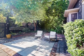 A patio with two white chairs, a black fence, and lush greenery. - Serene Studio 1st-Floor - Deck - Kitchenette (Seattle)