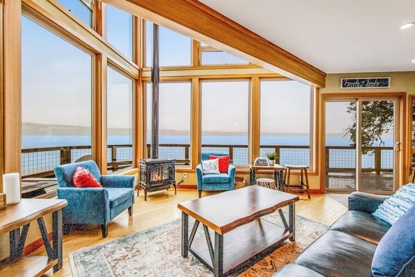 A spacious room with large windows, a fireplace, and a view of the water. - Stunning 3BR Oceanfront Dog Friendly - Dock (Tahuya)
