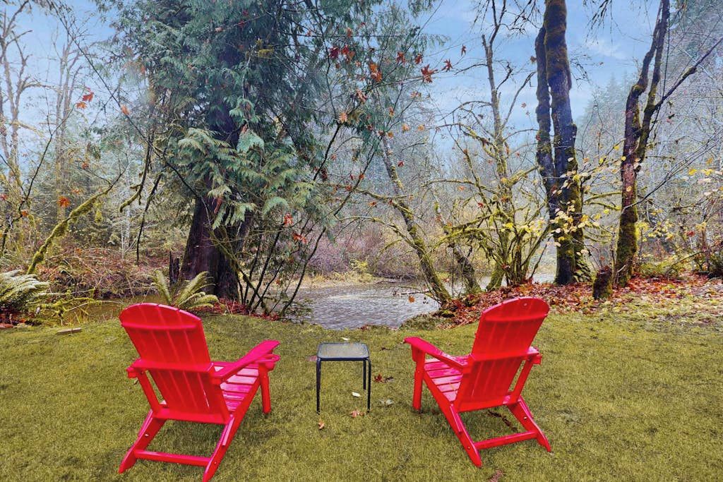 A grassy area with two red chairs and a small table, surrounded by trees and a body of water.