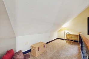 A room with a sloped ceiling, a small wooden chest, a chair, and a lamp.