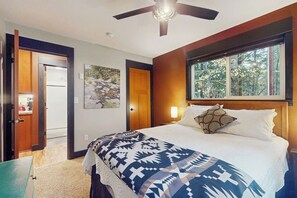 A bedroom with a bed, a ceiling fan, a window with a view of trees, and a door leading to another room. - 2BR withLoft Riverfront-Gas Grill-Wood Stove-Big Yard (Tahuya)