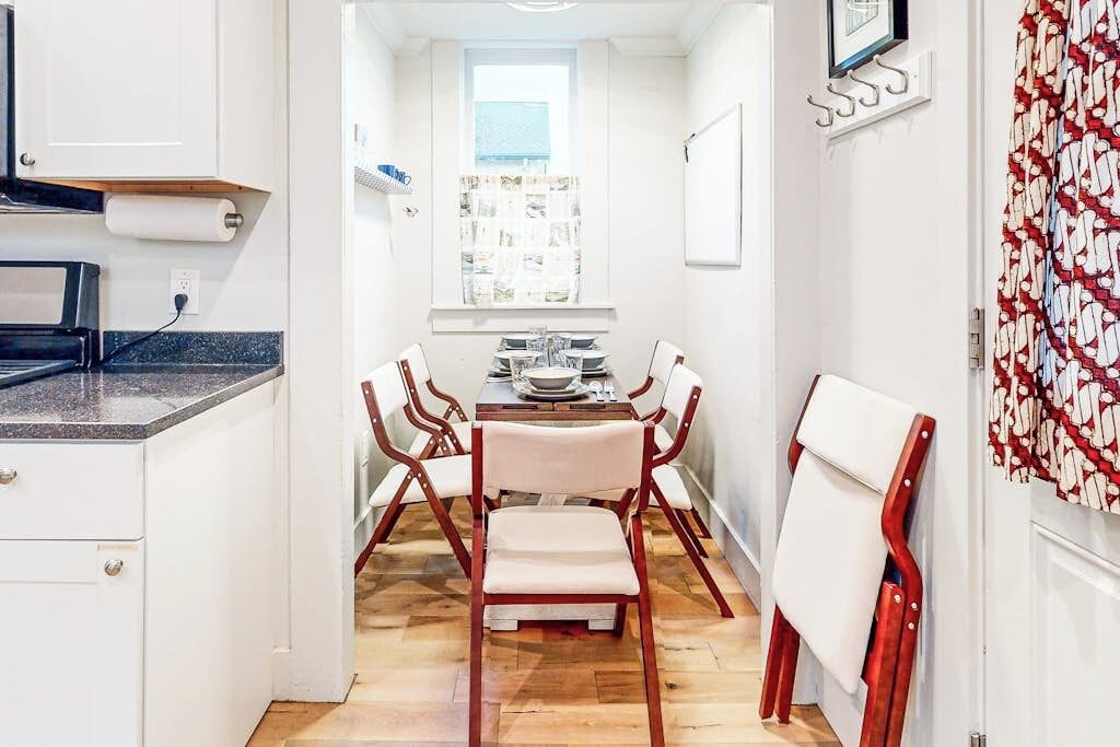 Una cocina compacta con comedor, piso de madera y muebles de cocina blancos.