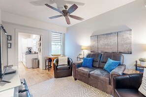 Un salon avec un canapé, une table basse, un téléviseur et un ventilateur de plafond.
