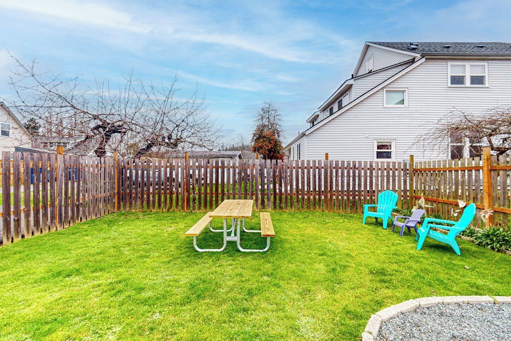 En baghave med et picnicbord og stole, et træhegn og et hus i baggrunden.