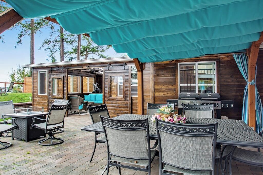 Une terrasse extérieure dotée d’un espace salon couvert, d’un barbecue et d’une table avec des chaises.
