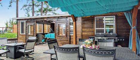 Une terrasse extérieure dotée d’un espace salon couvert, d’un barbecue et d’une table avec des chaises.