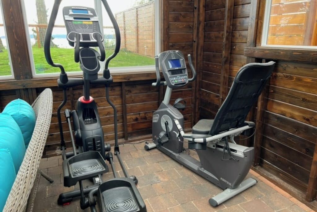 Ett hemmagym med träningsutrustning, inklusive en motionscykel, en crosstrainer och en stegmaskin.