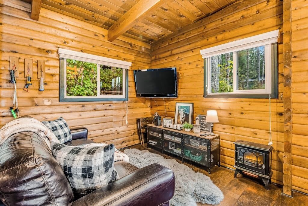 L’intérieur d’une cabane en rondins, avec un canapé en cuir, un téléviseur fixé au mur et une cheminée.
