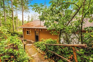 A wooden cabin with a door, surrounded by dense greenery and trees. - Dog-friendly 2BR lakefront cabin with amazing view (Tahuya)