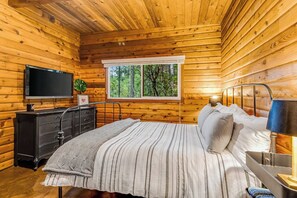 A wooden cabin bedroom with a bed, dresser, television, window, and lamp. - Dog-friendly 2BR lakefront cabin with amazing view (Tahuya)