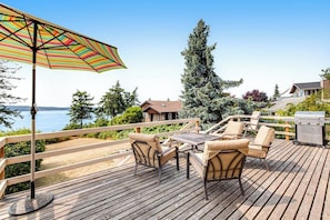 A wooden deck with outdoor furniture, a grill, and a view of the water. - Large 2BR Oceanfront - Deck - Firepit - Washer Dryer (Camano Island)