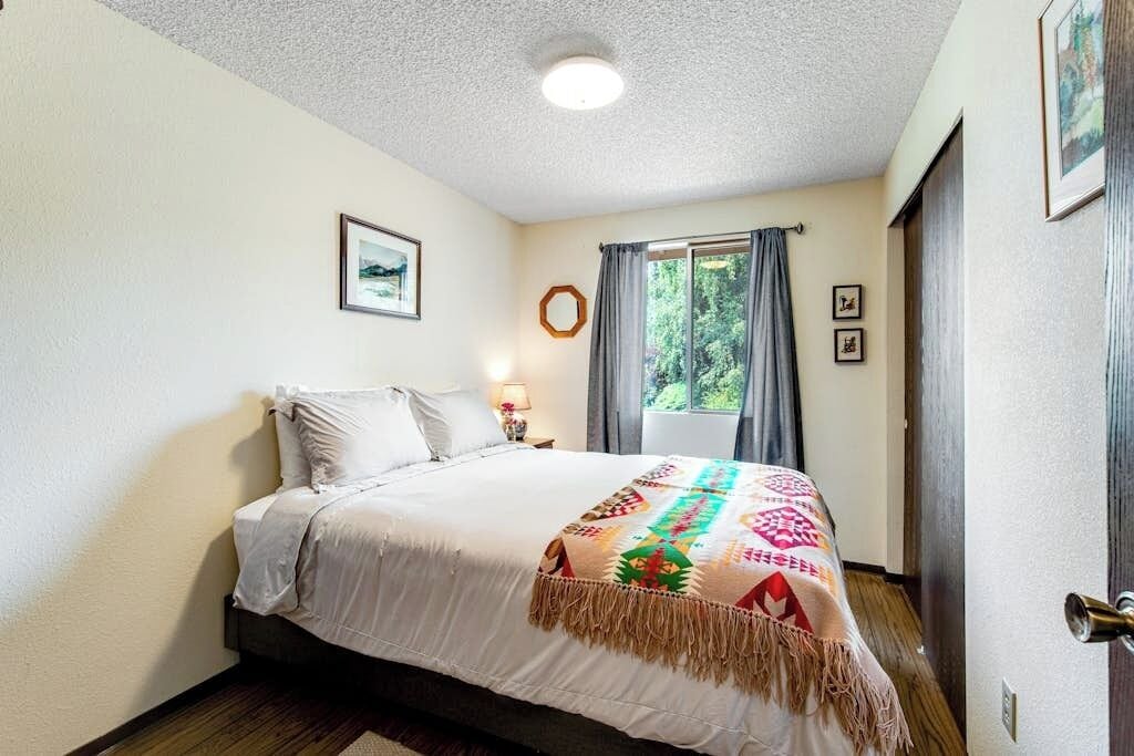 A bedroom with a bed, a window with curtains, a wall-mounted picture, and a door.