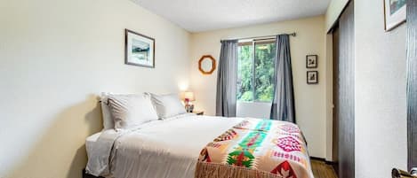 A bedroom with a bed, a window with curtains, a wall-mounted picture, and a door.