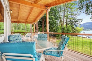 Un espace extérieur abrité, avec une table et des chaises, offrant une vue sur un lac et un paysage boisé.