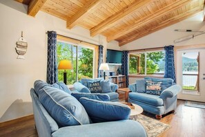 A living room with a high ceiling, two sofas with matching cushions, a small table, and a lamp. - 2BR Lakefront - Dock - WoodStove - Deck (Bellingham)