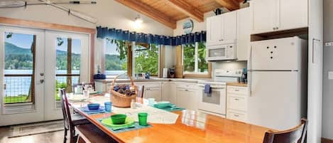 Una cocina con una mesa de madera, armarios blancos y vistas al exterior.