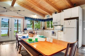 A kitchen with a wooden table, white cabinets, and a view of the outdoors. - 2BR Lakefront - Dock - WoodStove - Deck (Bellingham)