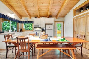 A wooden dining table with chairs, a bench, and a kitchen area with cabinets and appliances. - 2BR Lakefront - Dock - WoodStove - Deck (Bellingham)