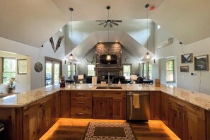 A spacious kitchen with a large island, wooden cabinets, and a stone fireplace. - 4BR Home with fire pit & pickleball and basketball court (Cle Elum)