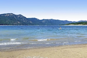 Ein Strand mit klarem Wasser, eine Person im Wasser und Berge im Hintergrund.