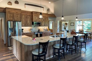 A spacious kitchen with wooden cabinets, a central island with bar stools, stainless steel appliances, and pendant lighting. - 4BR Home with fire pit & pickleball and basketball court (Cle Elum)