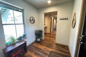 Ein Flur mit Holzboden, Kamin, Blumentopf, Kleiderständer und Spiegel an der Wand.