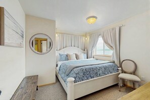 Une chambre à coucher avec un lit, une chaise, un miroir et une fenêtre avec des rideaux.