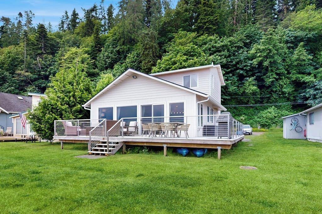 A two-story house with a deck, a staircase, and a small shed in a grassy yard.