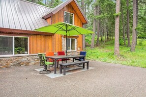 Eine Holzhütte mit Steinfundament, eine Terrasse mit Tisch und Stühlen und einem grünen Sonnenschirm.